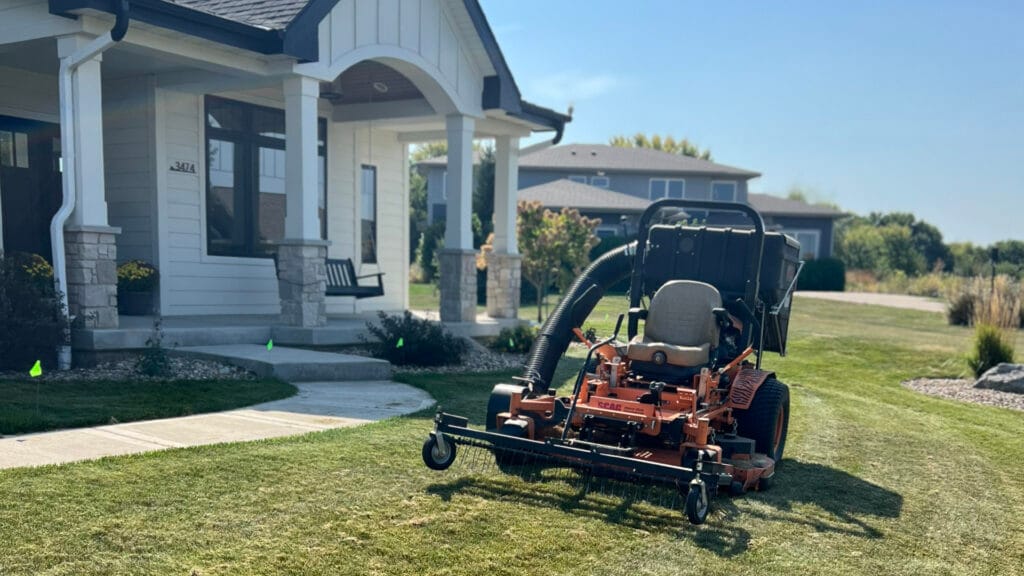 a lawn mower with a thatching attachment going across a lawn