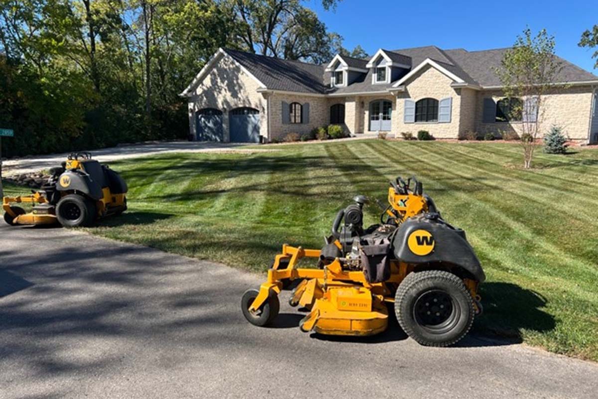 two lawnmowers outside a large house