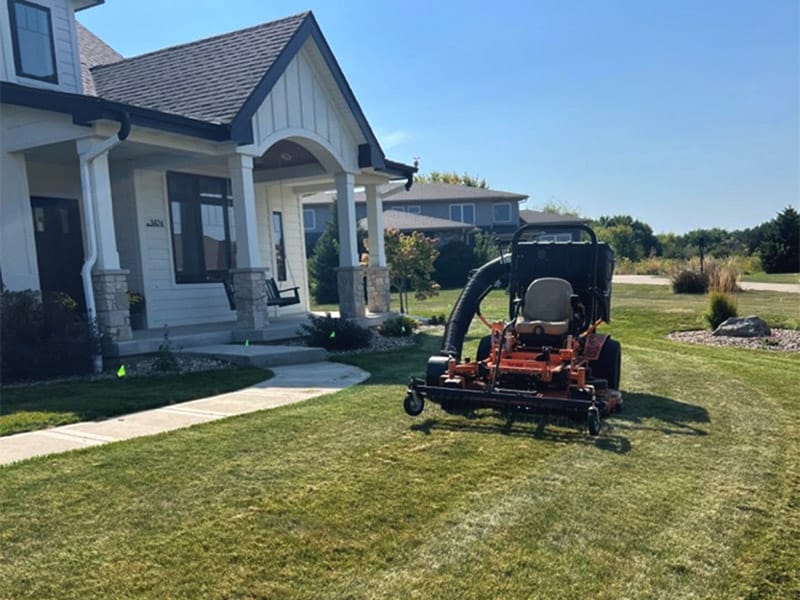 a lawn mower with a thatching attachment going across a lawn
